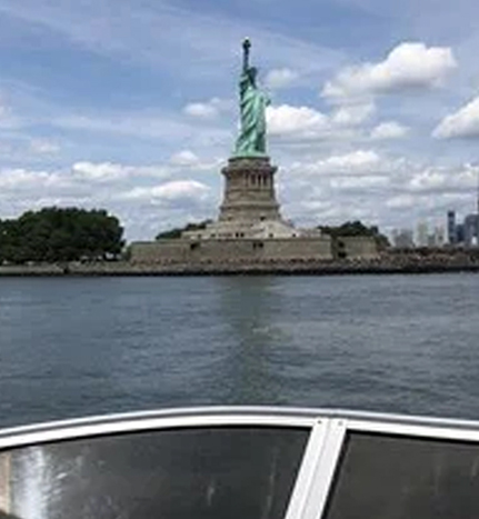 A boat is traveling on the water near a statue of liberty.