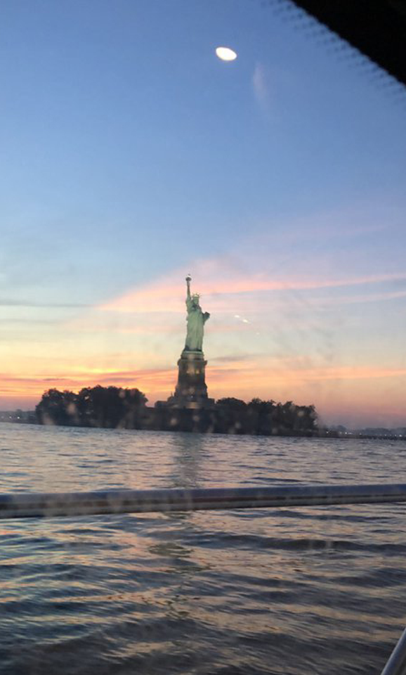 A statue of liberty is seen from the water.